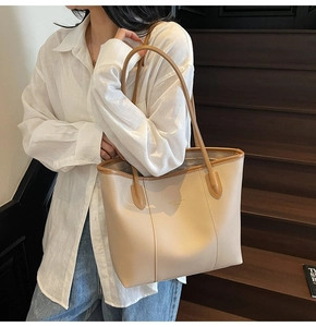 Detail view of cream tote bag with brown straps worn on shoulder in stylish setting