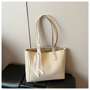 Close-up of beige tote bag with woven texture, leather handles and decorative silk scarf