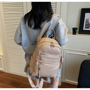 Rear view of model wearing a beige pebbled faux leather backpack with silver zippers