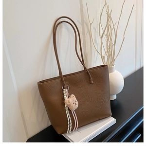 Detail of brown lychee grain leather tote bag featuring a cute teddy bear charm