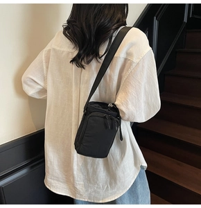 Rear view of a black nylon drawstring crossbody bucket bag worn on a minimalist backdrop