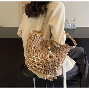 Detail of woven straw tote bag featuring ethnic tassel charm with blue and white beads