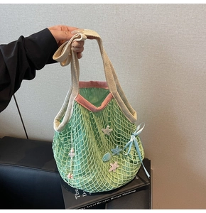 Detail of green knit tote bag with mesh design, pink handles and star shell charms