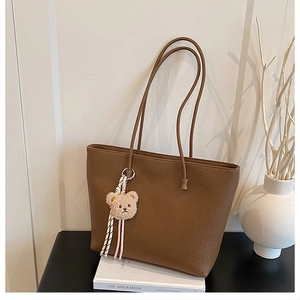 Detailed view of dark brown pebbled leather tote bag with a plush bear charm ornament