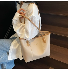 Close-up of a beige faux leather tote bag with brown straps worn by a model on stairs