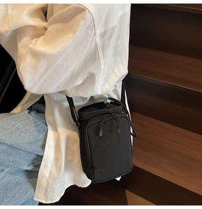 Close-up of black nylon drawstring crossbody bag worn by a model in casual setting