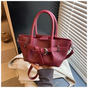 Détail du sac seau en cuir bordeaux avec boucle décorative et bandoulière réglable