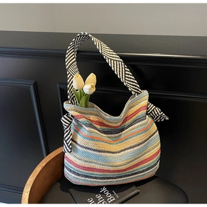 Dettaglio della borsa tote in paglia a righe colorate con manici geometrici su una sedia
