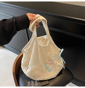 Close-up of cream knit tote bag featuring colorful star charms and blue silk bow detail