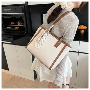 Detail of off-white woven tote bag with brown leather trim and decorative checkered scarf