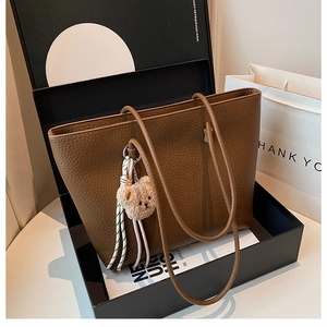 Close-up of brown litchi pattern leather tote bag with plush bear charm in a gift box