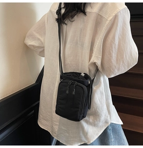 Close-up of black nylon drawstring crossbody bag with double front zippers on a model