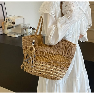 Detail of woven straw tote bag featuring decorative blue beads and wooden ring tassel
