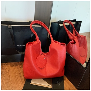 Détail d'un grand sac cabas rouge en cuir grainé avec un pendentif rond décoratif
