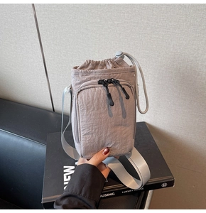 Close-up of light gray nylon drawstring bag with front zipper pocket and adjustable strap