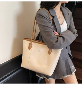 Model wearing a large cream tote bag with brown handles and PU leather finish