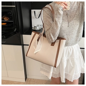 Detail of a large cream woven tote bag with brown leather straps and decorative scarf
