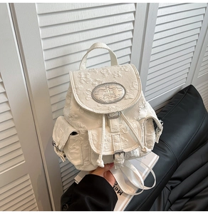 Detail eines weißen Jacquard-Rucksacks mit floralem Prägestoff und silberner Metallplakette