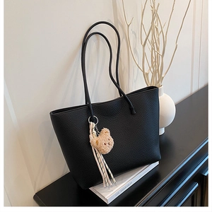 Detail of black pebbled leather tote bag with plush bear charm and striped tassel accessory