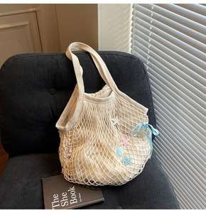 Detail of cream woven tote bag with starfish charms and bow on a dark velvet chair