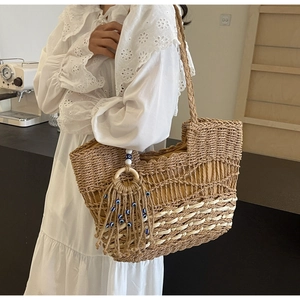 Close-up of woven straw tote bag featuring hollow diamond pattern and tassel charm