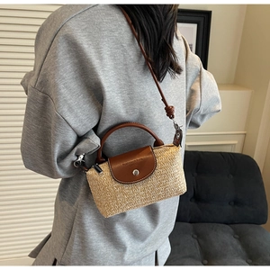 Close-up of woven straw texture and brown leather flap with metal buckle on crossbody bag