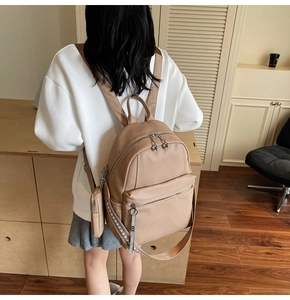 Detail view of khaki leather backpack with multiple zippers and mini coin purse attachment