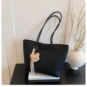 Detail of black lychee grain leather tote bag with a cute brown plush bear charm