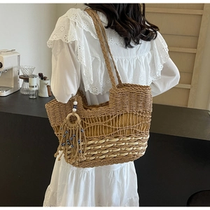 Detail of woven straw tote bag featuring intricate cut-out patterns and bead tassels