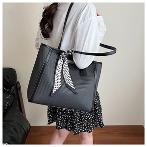 Close-up of black woven tote bag with a geometric print silk scarf and long shoulder strap