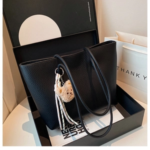 Close-up of black lychee grain leather tote bag with bear charm in a luxury gift box