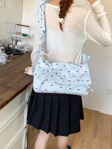 Sac à bandoulière bleu à motifs nœuds rouges avec sangle plissée porté par un modèle