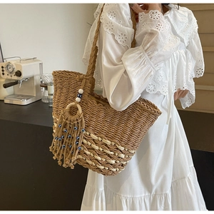 Detail of woven straw tote bag with evil eye tassel charm and white wave stripe patterns