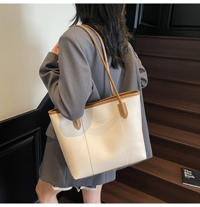 Detail of a cream tote bag with brown trim and long straps in a modern minimalist setting