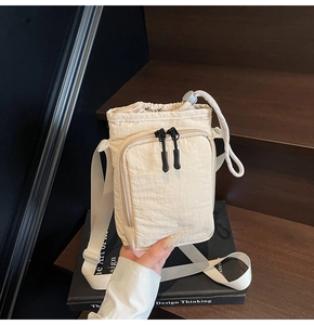 Detail of minimalist cream nylon drawstring bucket bag with dual zippers and woven strap