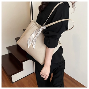 Close-up of beige woven tote bag featuring a leather trim and a silk scarf decoration
