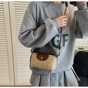 Detail view of woven straw crossbody bag with brown leather flap and metal snap button