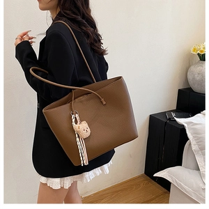 Brown lychee grain leather tote bag shown on a model with cute bear plush charm