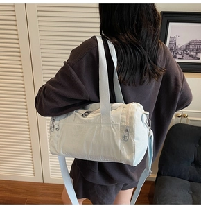 Modern light blue nylon duffle bag worn over the shoulder by a model in a home setting
