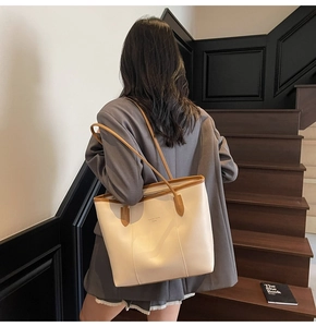 Detail of a large cream tote bag with brown straps styled on a person in a warm setting