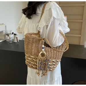 Detail of hand-woven straw tote bag with evil eye tassel charm on bohemian shoulder bag
