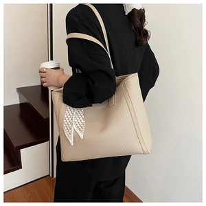 Detail of beige woven tote bag featuring a geometric silk scarf handle on model