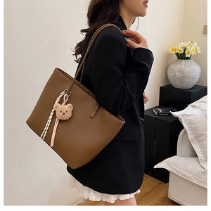 Close-up of brown litchi pattern leather tote bag with a cute plush bear charm decoration