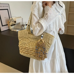 Detail of hollow woven straw tote with evil eye tassel and wood ring accessory