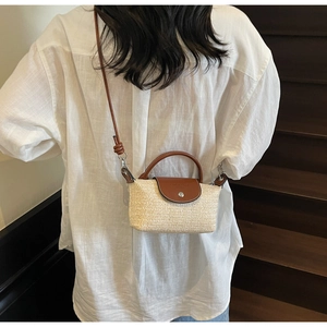 Detail of hand-woven straw crossbody bag with brown leather flap and handle on a model