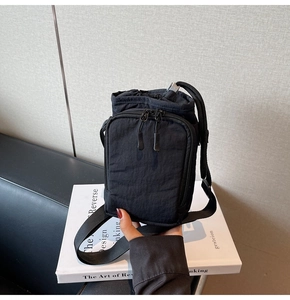 Detail of black nylon mini crossbody bag with drawstring closure and front zip pocket
