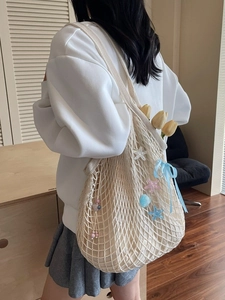 Beige hand-woven tote bag with blue ribbons and star charms worn by a model in soft lighting