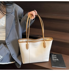 Detail of cream tote bag with brown handles being held against a wooden background