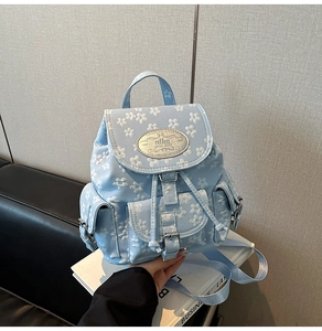 Detailansicht hellblauer Blumenrucksack mit silbernem Logo-Schild und Kordelzug