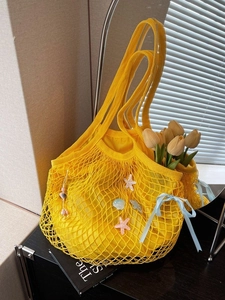 Yellow woven tote bag with sea-themed charms and blue bow in bright summer lighting